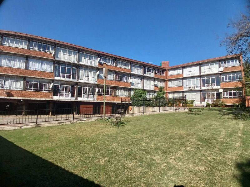 A view of the rear exterior of a multi-story brick apartment building featuring balconies and a shared lawn area.