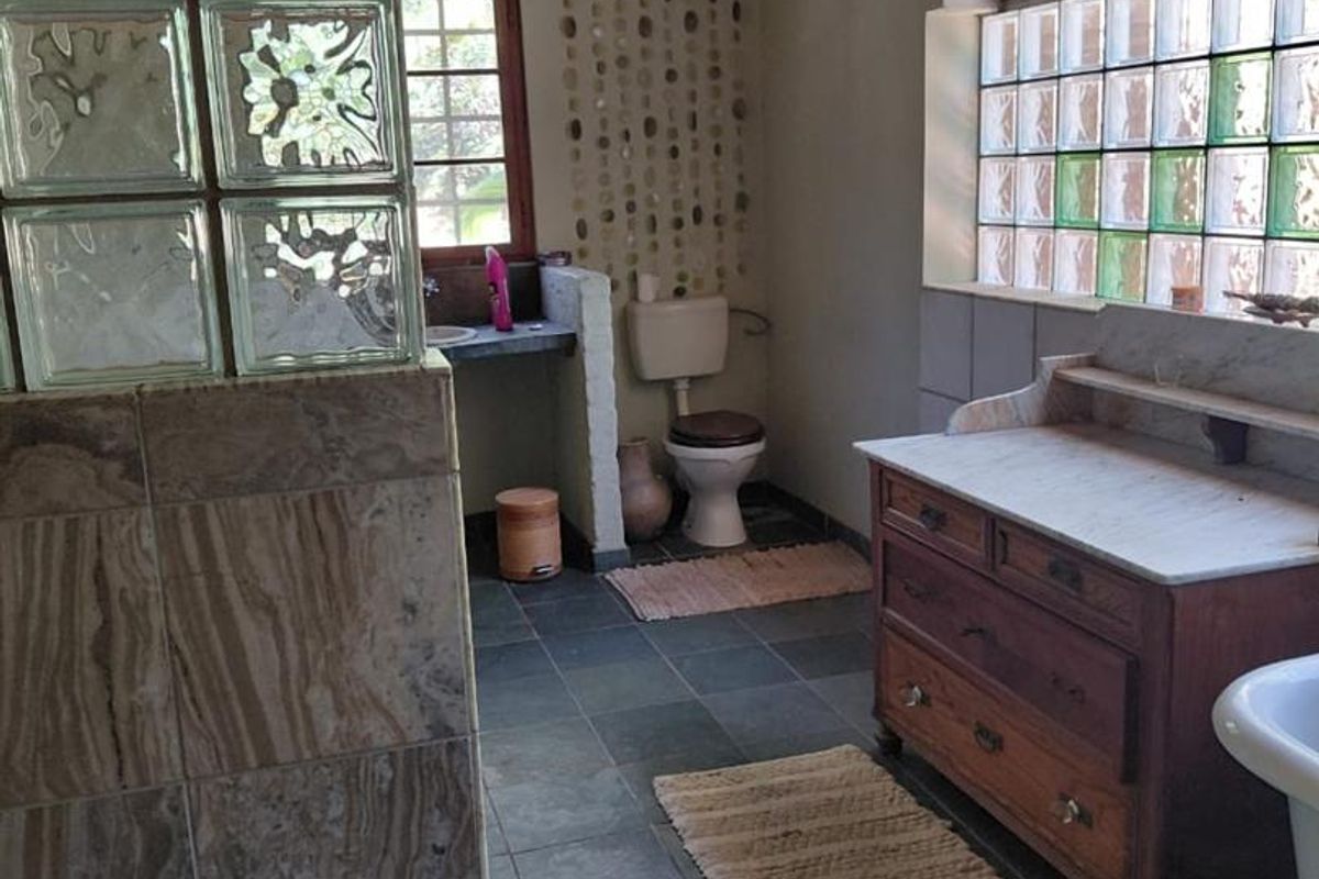 A rustic-style bathroom featuring slate flooring, a glass block partition, a stone-topped vanity, and a unique thatched ceiling.