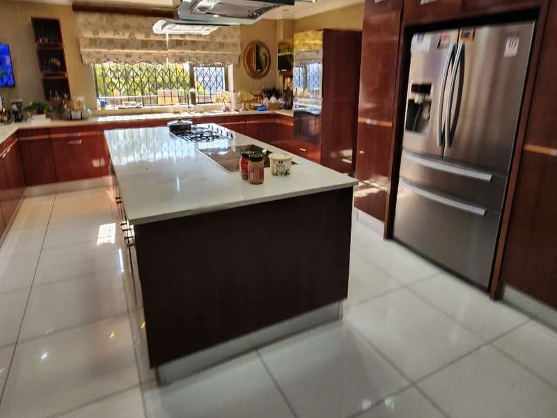 Modern kitchen featuring a central island with stone countertops, high-gloss cabinetry, integrated stainless steel appliances, and polished tile flooring.