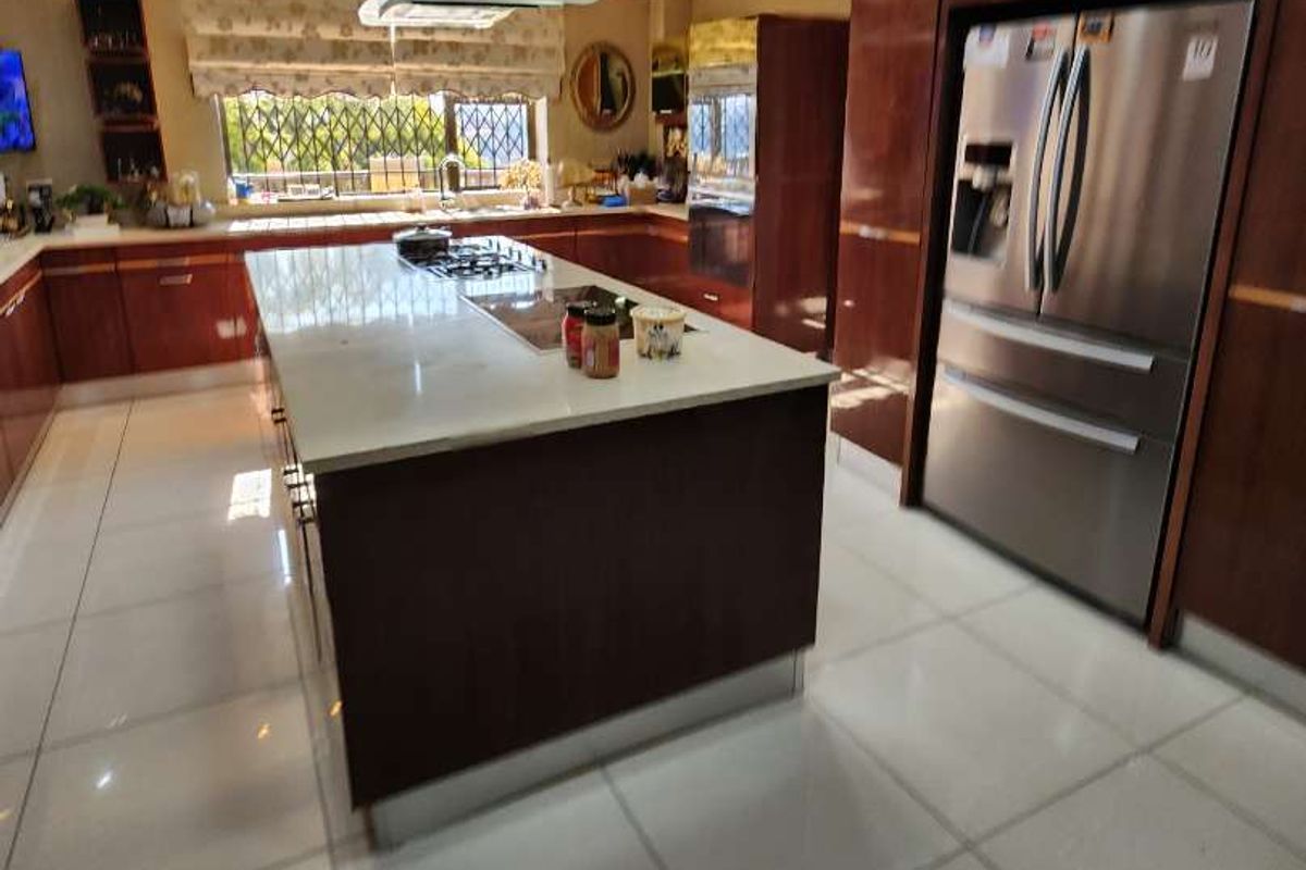 Modern kitchen featuring a central island with stone countertops, high-gloss cabinetry, integrated stainless steel appliances, and polished tile flooring.