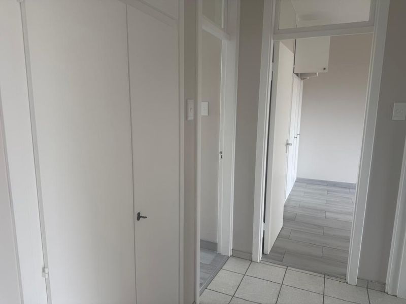 A clean, neutral hallway featuring tiled flooring and multiple built-in cupboard doors, providing a bright and functional transition space within the townhouse.
