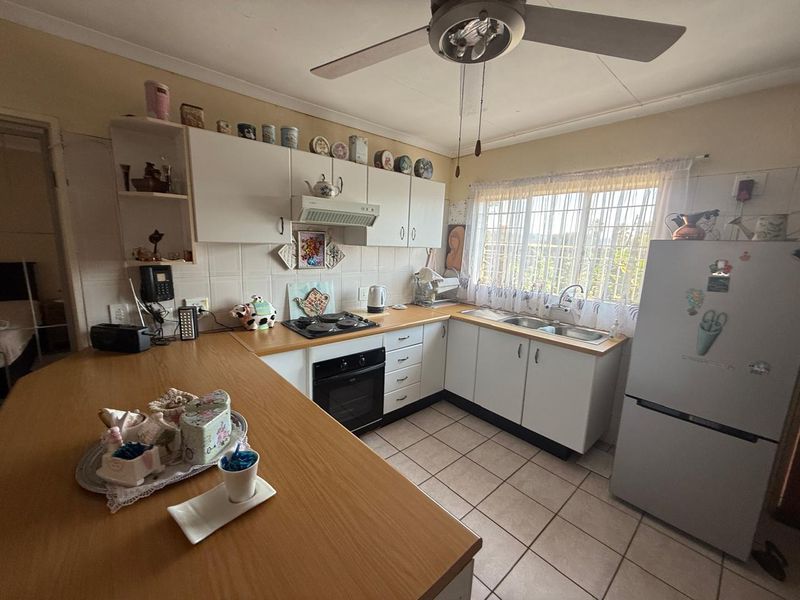 Functional kitchen featuring built-in cabinetry, laminate countertops, integrated oven and hob, double sink, and tiled flooring with a ceiling fan.