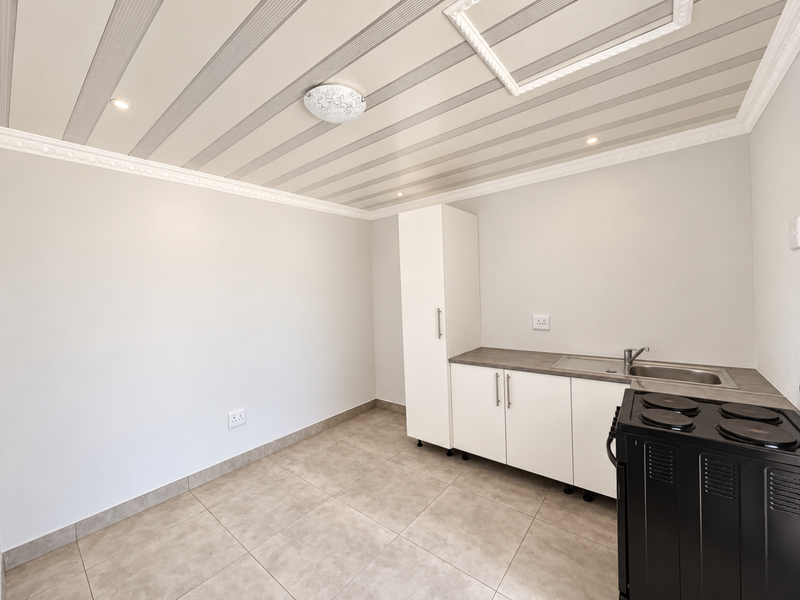 A clean, modern kitchen area featuring built-in cabinetry, a stainless steel sink, and an electric stove, set against neutral walls and tiled flooring.