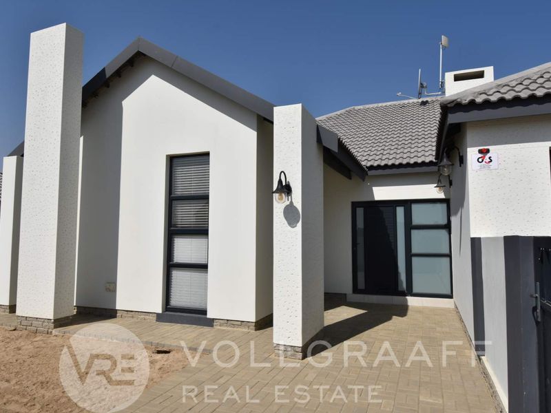 Modern front facade featuring clean white rendered walls, tiled roofing, paved entrance area, and contemporary aluminium window frames.