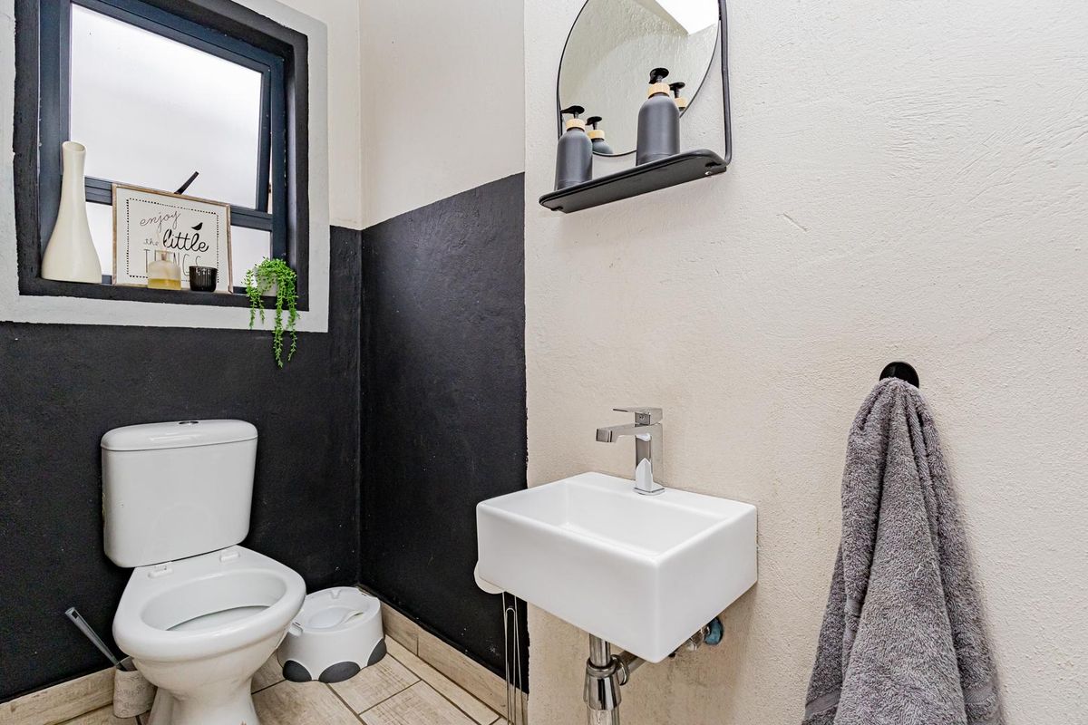 A compact guest bathroom featuring a modern wall-mounted basin, chrome mixer, and a standard toilet with tiled flooring and a top-hung window.