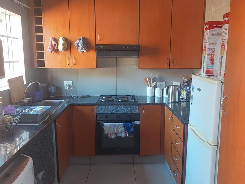 Compact kitchen featuring wooden cabinetry, granite countertops, built-in oven, electric hob, and tiled flooring.