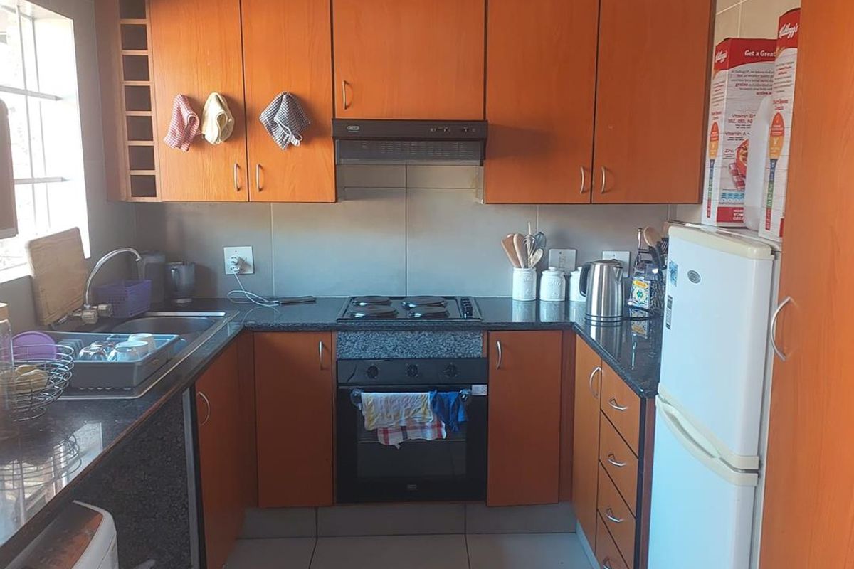 Compact kitchen featuring wooden cabinetry, granite countertops, built-in oven, electric hob, and tiled flooring.