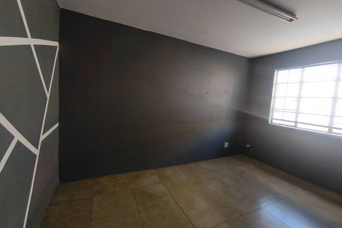 An empty bedroom featuring dark painted walls with geometric accents, tiled flooring, and a window with fitted blinds.
