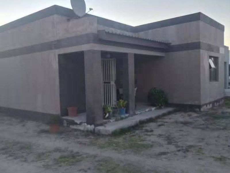 A single-story residential property featuring a covered front porch, security gate, and satellite dish, set on an undeveloped plot.