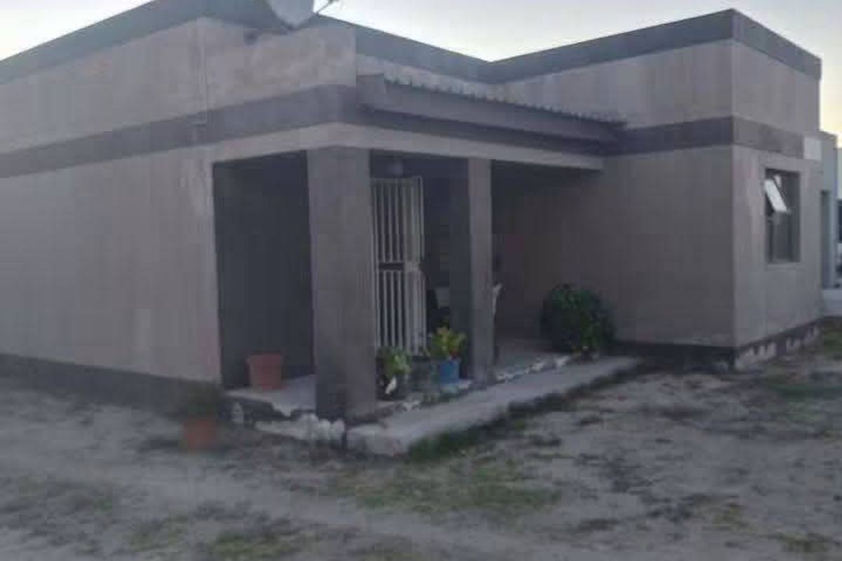 A single-story residential property featuring a covered front porch, security gate, and satellite dish, set on an undeveloped plot.