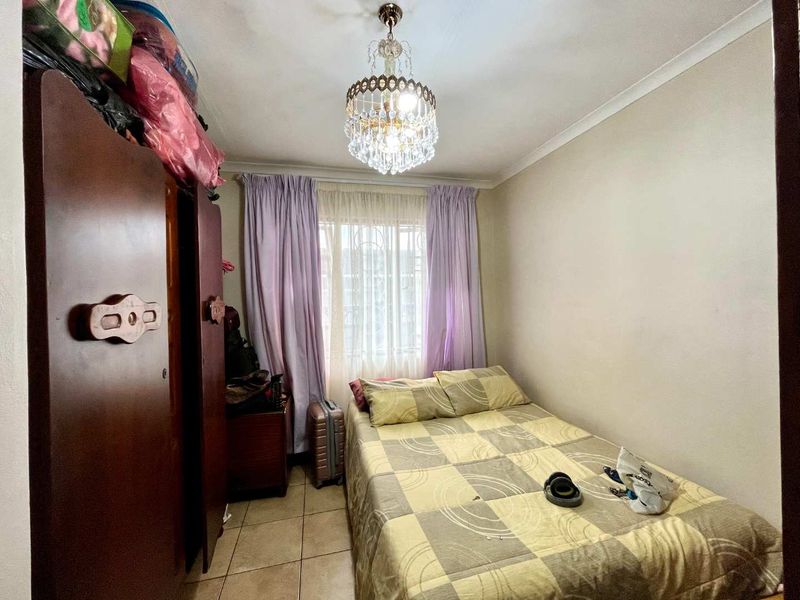 A compact bedroom featuring tiled flooring, a decorative crystal chandelier, and a window fitted with security bars.