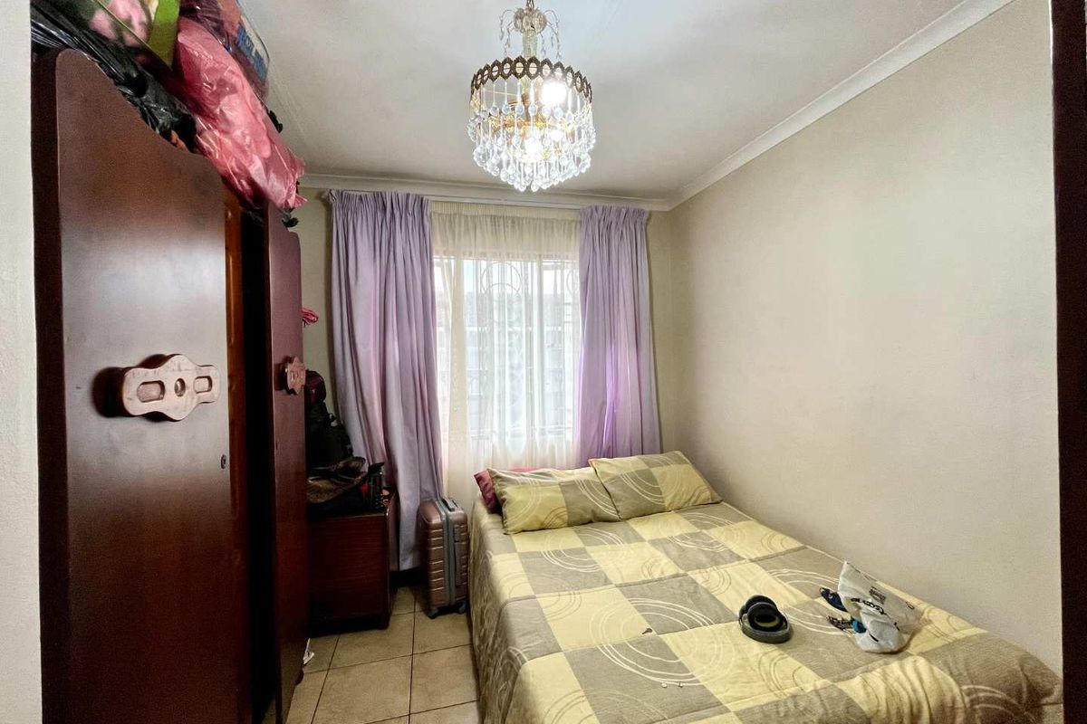 A compact bedroom featuring tiled flooring, a decorative crystal chandelier, and a window fitted with security bars.