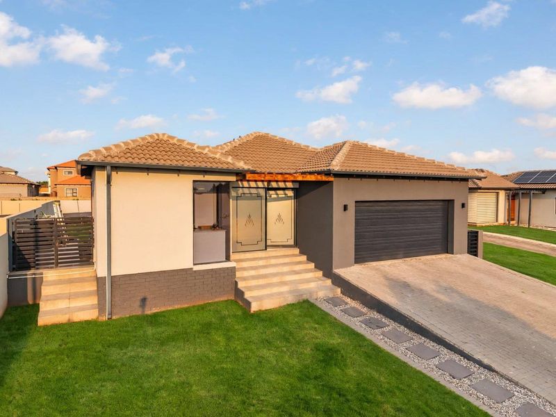 Modern single-story house featuring a double garage, paved driveway, and a well-maintained front garden with concrete entrance steps.