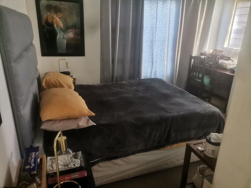 A functional bedroom featuring neutral walls, window treatments including curtains and blinds, and space for a bed and desk area.