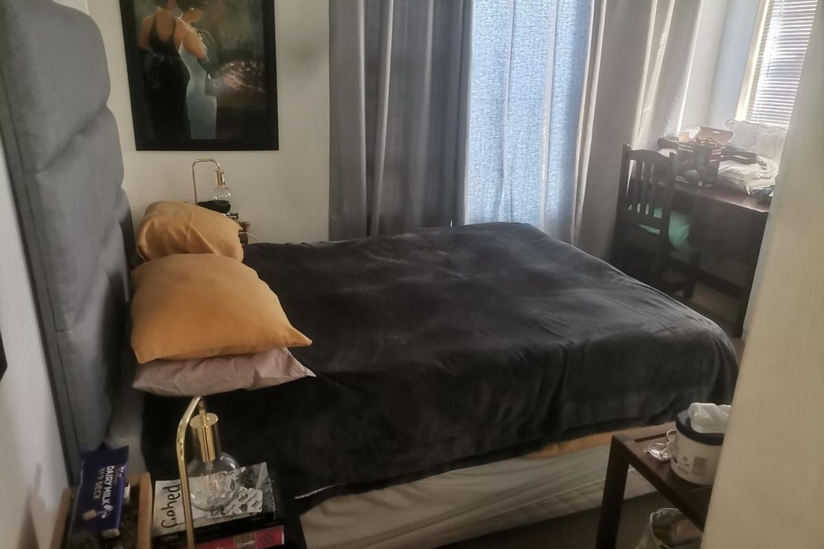 A functional bedroom featuring neutral walls, window treatments including curtains and blinds, and space for a bed and desk area.
