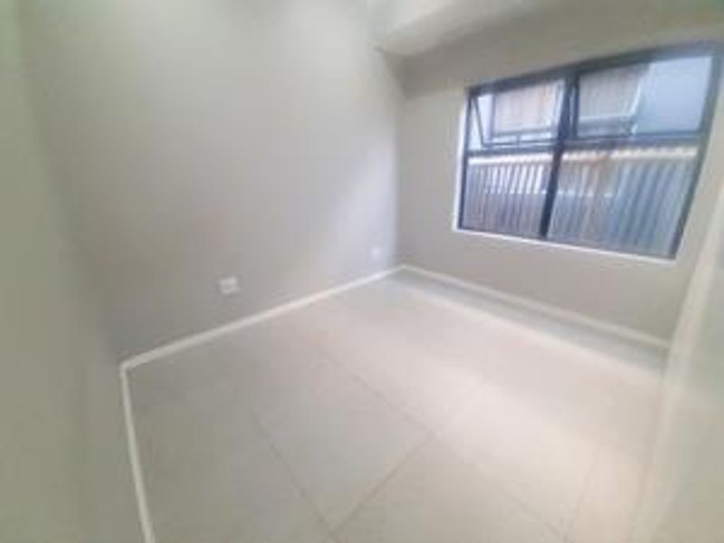 A clean, empty bedroom featuring neutral tiled flooring and a modern aluminium-framed window, providing a bright and versatile space.