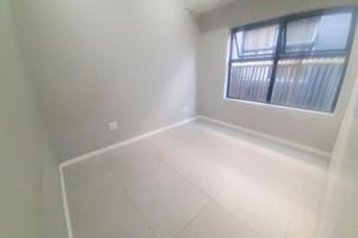A clean, empty bedroom featuring neutral tiled flooring and a modern aluminium-framed window, providing a bright and versatile space.