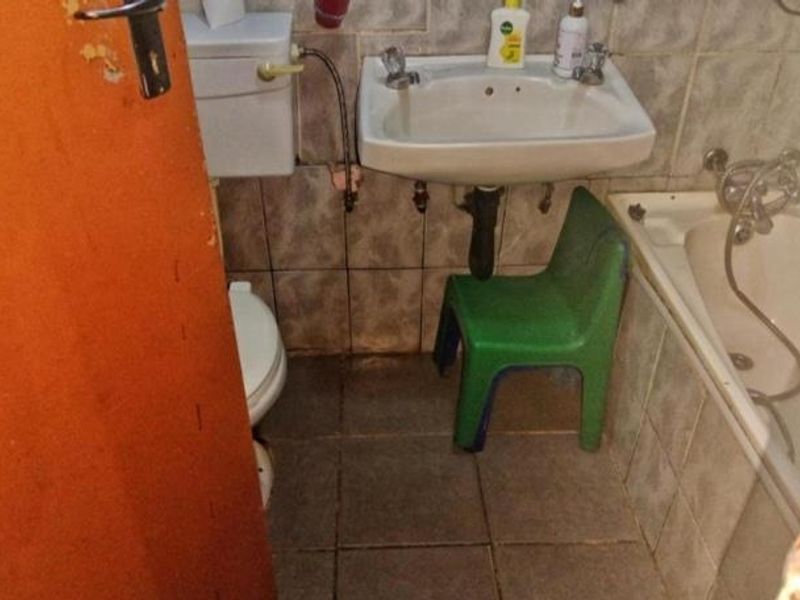A compact bathroom featuring a wall-mounted basin, toilet, and bathtub with dated tiled finishes throughout.