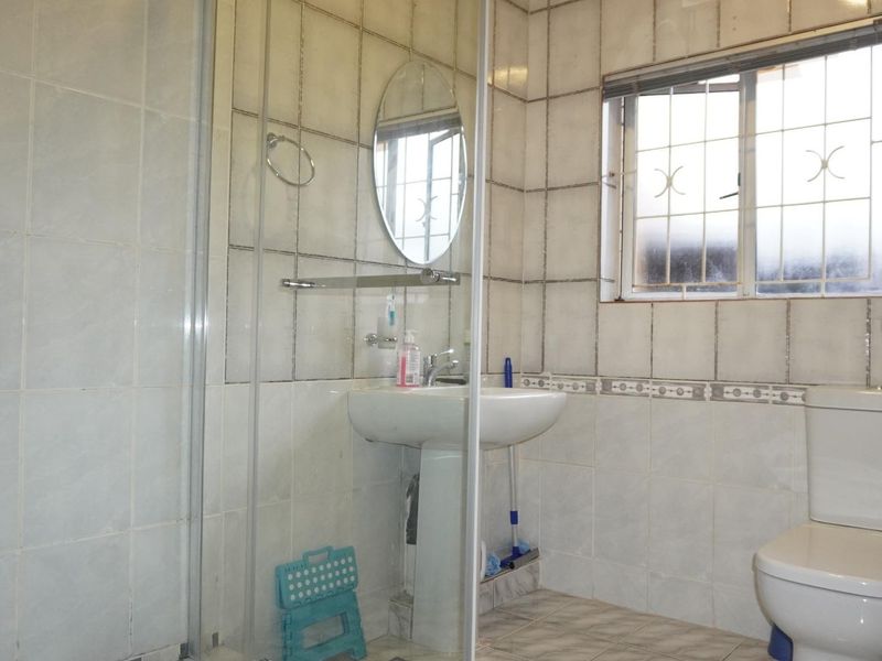 A dated bathroom featuring a pedestal basin, a shower enclosure, and ceramic tiling throughout, requiring modernization to improve its aesthetic appeal.