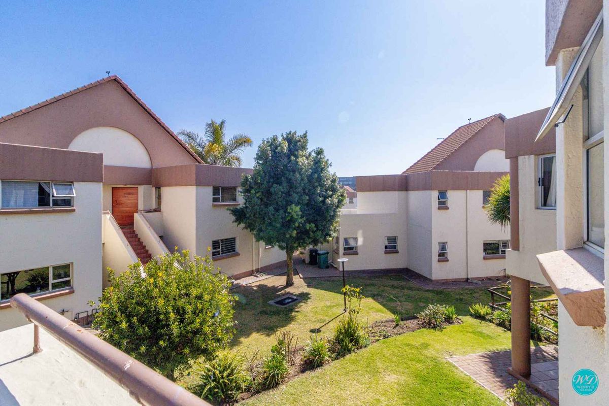 A view of the apartment complex courtyard featuring a landscaped garden, paved walkways, and exterior building facades with tiled roofing.