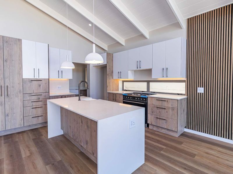 Modern kitchen featuring a central island, quartz countertops, built-in oven, gas hob, and stylish slatted wood feature wall under exposed ceiling beams.