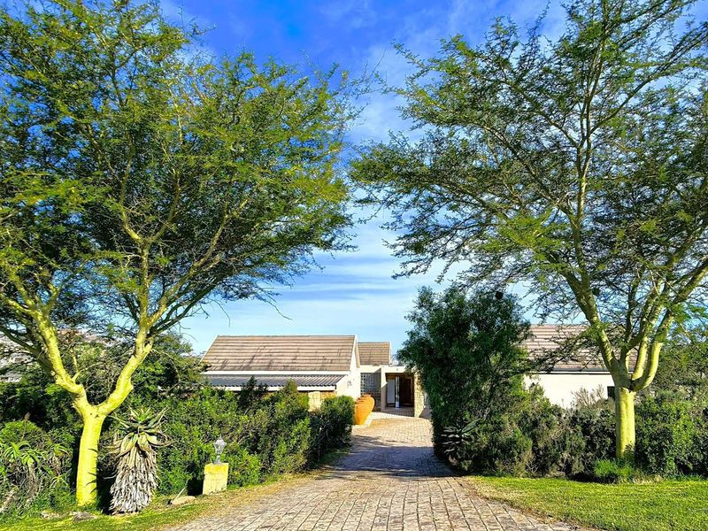 A well-maintained front exterior view of the house featuring a paved driveway leading to the entrance, surrounded by mature trees and landscaped gardens.