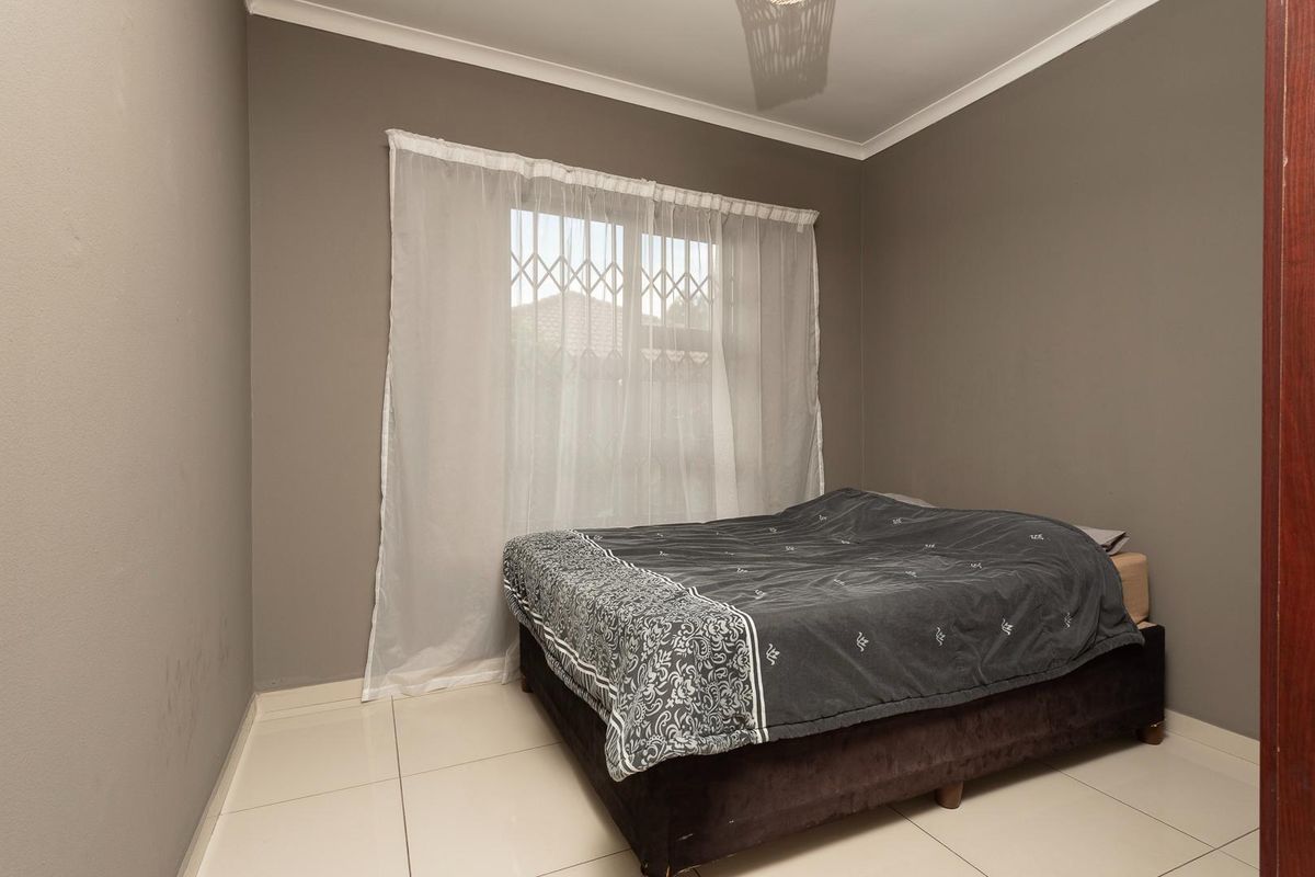A bedroom featuring neutral grey walls, tiled flooring, and a window fitted with security bars.