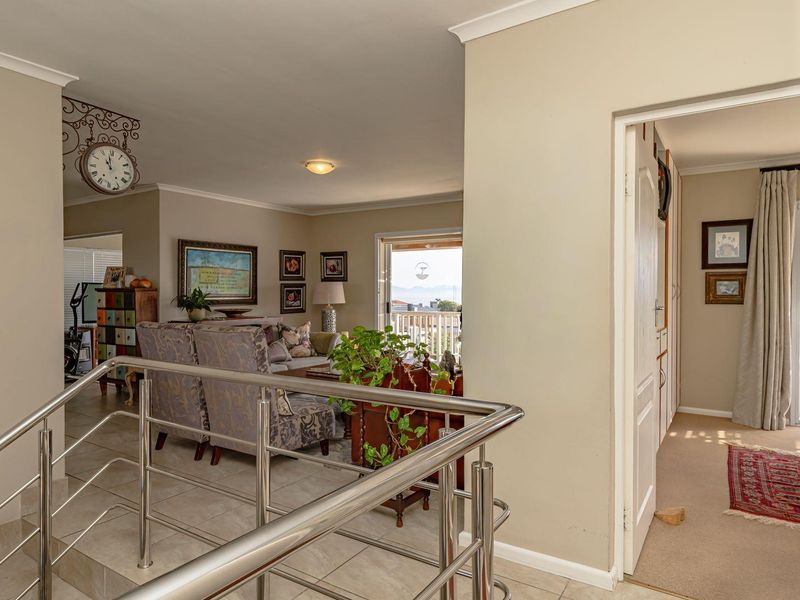 A bright hallway featuring a modern stainless steel balustrade, tiled flooring, and access to the living area and adjacent bedroom.