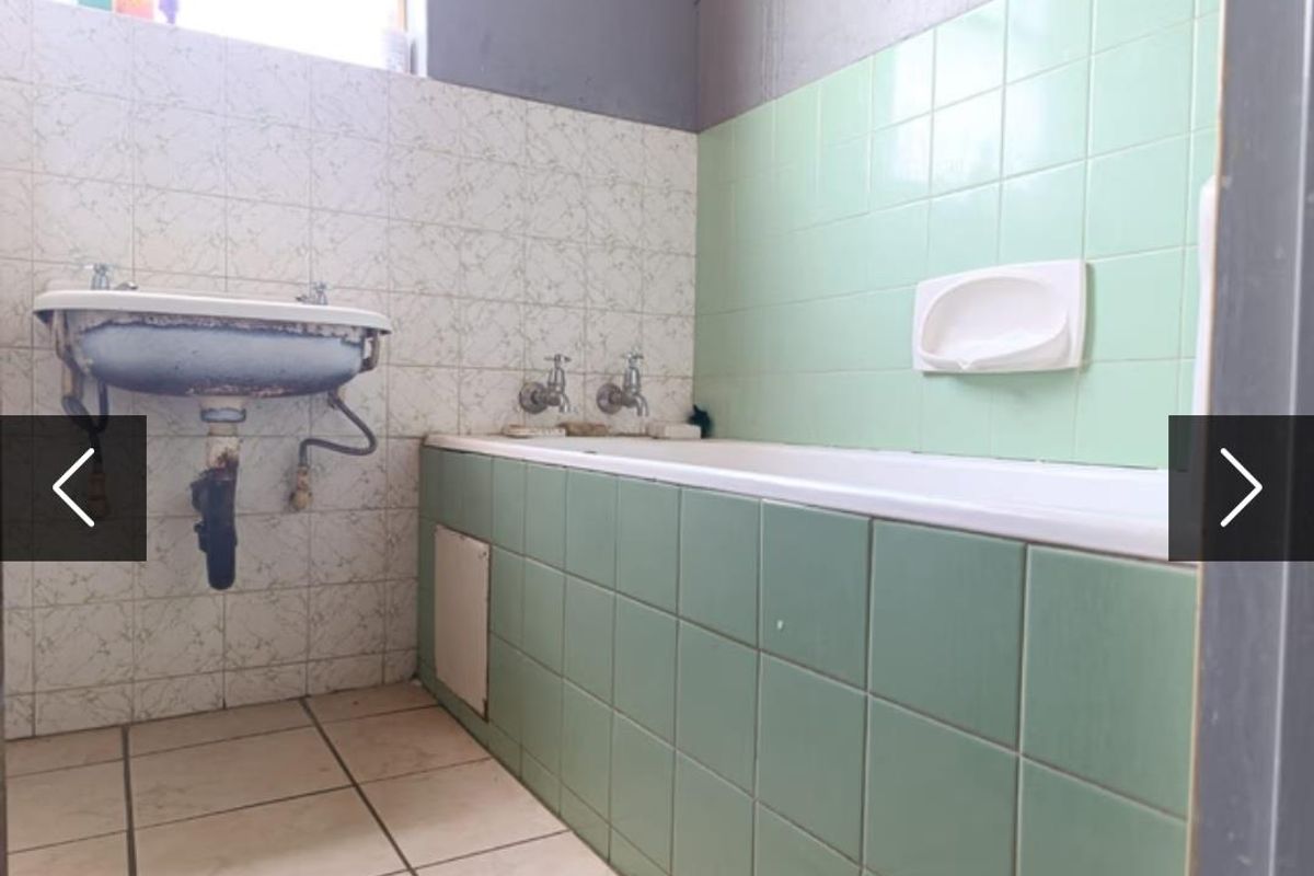 A dated bathroom featuring a wall-mounted basin and a tiled bathtub, requiring significant renovation and modernization of fixtures and finishes.