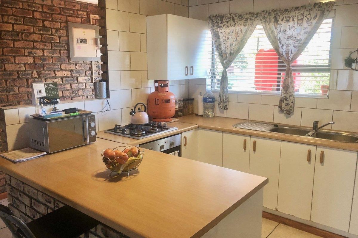 A functional kitchen featuring a gas hob, built-in oven, stainless steel sink, and a breakfast counter with exposed brick accents and tiled backsplash.