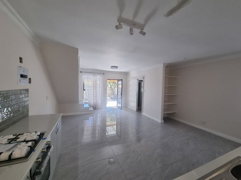 Spacious open-plan living area featuring tiled flooring, built-in kitchen appliances, and integrated shelving, leading out to an exterior patio area.