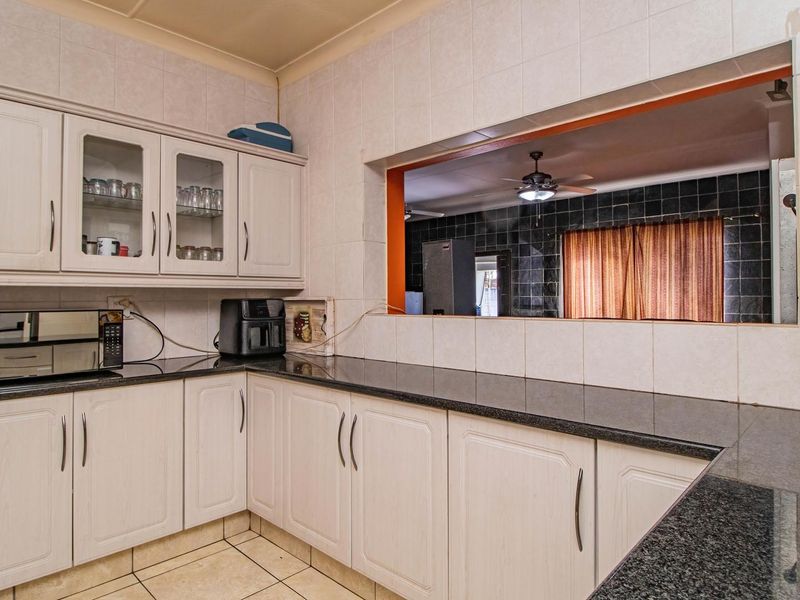 A functional kitchen featuring light-toned cabinetry, dark granite countertops, and a large serving hatch opening into the adjacent living area.