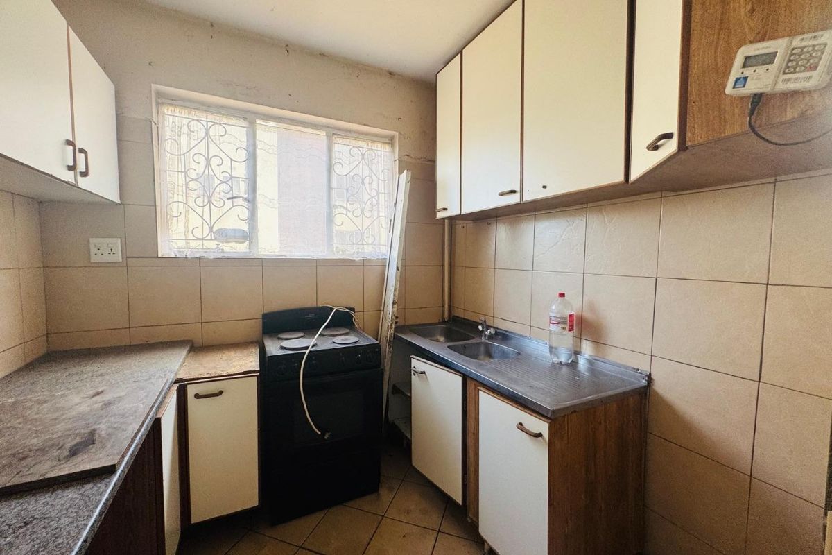 A dated kitchen featuring original cabinetry, tiled splashbacks, and a stainless steel sink, requiring modernization and cosmetic updates to improve functionality and aesthetic appeal.