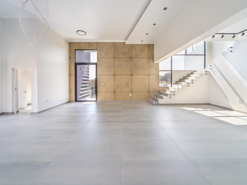 Spacious, modern open-plan living area featuring large format floor tiles, a striking floating staircase, and a contemporary feature wall with recessed lighting.
