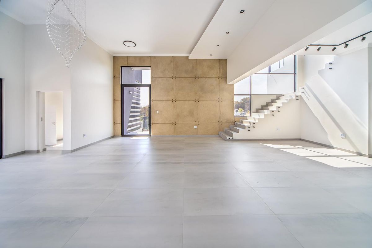 Spacious, modern open-plan living area featuring large format floor tiles, a striking floating staircase, and a contemporary feature wall with recessed lighting.