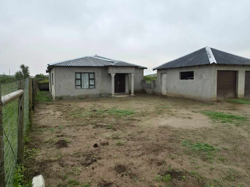Front view of a residential property featuring a main house and a detached double garage with unfinished exterior walls and unpaved grounds.