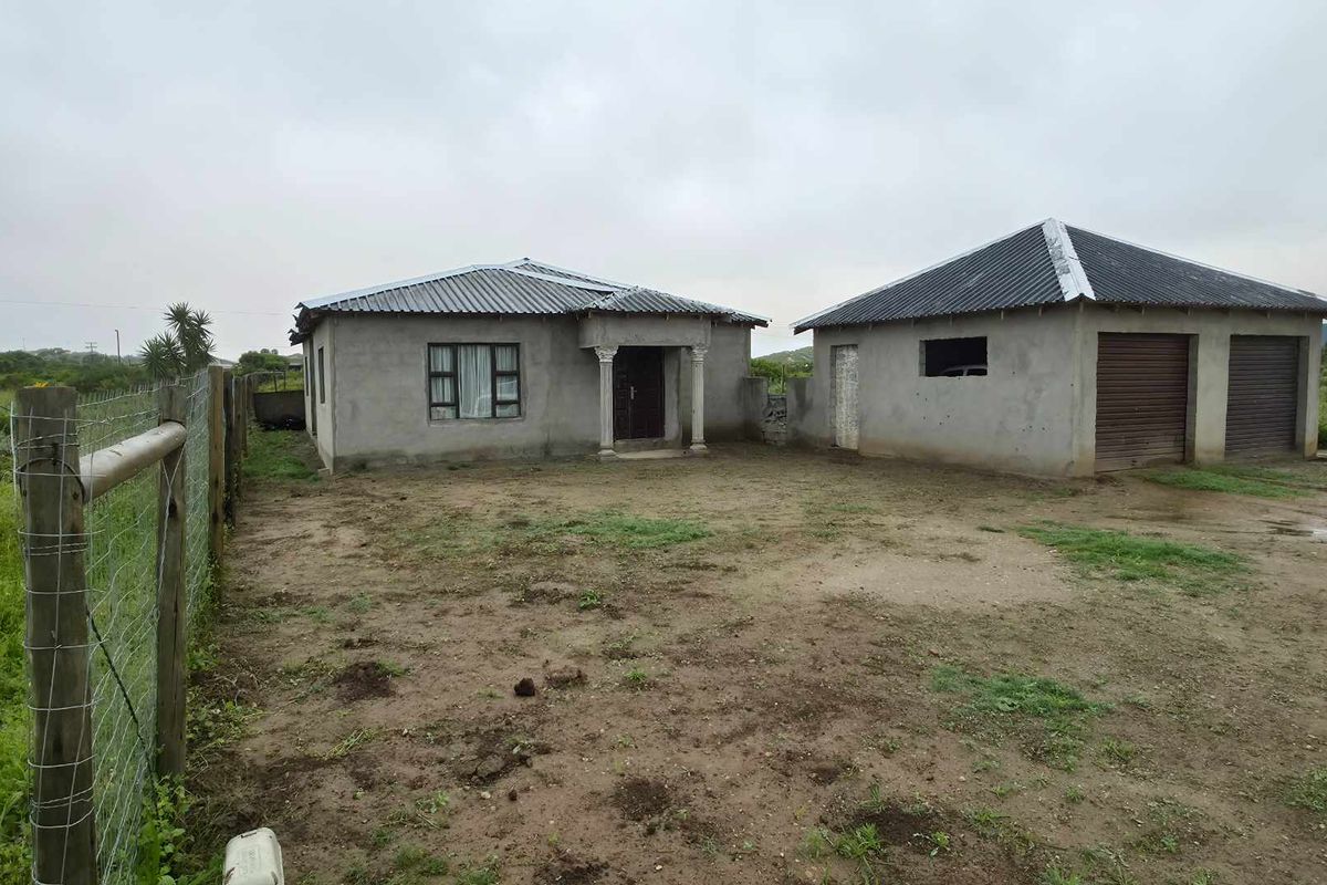 Front view of a residential property featuring a main house and a detached double garage with unfinished exterior walls and unpaved grounds.