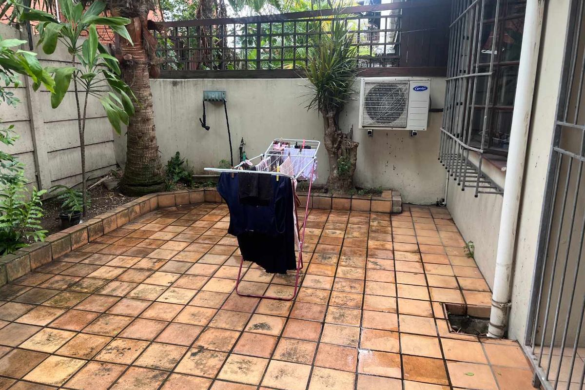 A private rear courtyard featuring tiled flooring, a boundary wall with trellis fencing, and an external air conditioning unit.