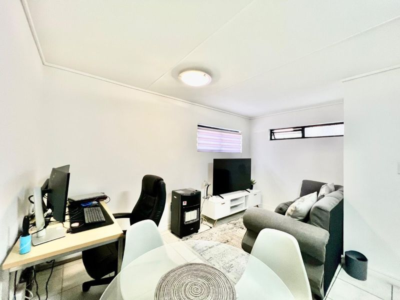 A functional living area featuring tiled flooring and horizontal windows, currently utilized as a multi-purpose space for relaxation and work.