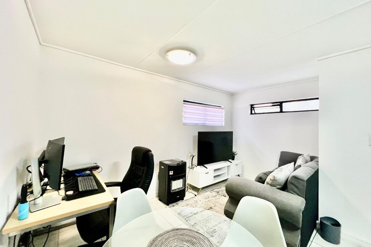A functional living area featuring tiled flooring and horizontal windows, currently utilized as a multi-purpose space for relaxation and work.
