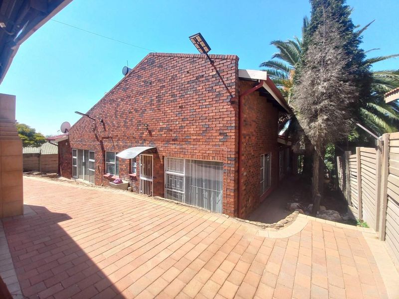 Rear exterior view of the house featuring a brick facade, paved patio area, and secure aluminum window frames.