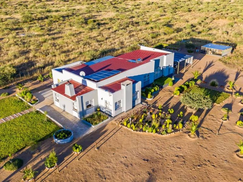 Aerial view of a detached house featuring a metal roof with integrated solar panels, set within a spacious, landscaped rural property.