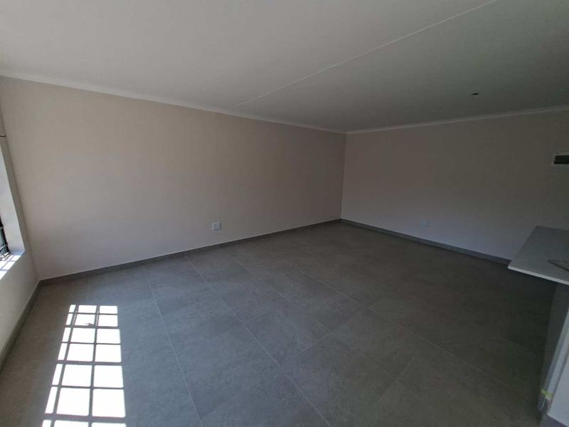 A spacious, empty open-plan living area featuring neutral walls, modern grey floor tiles, and natural light from a side window.
