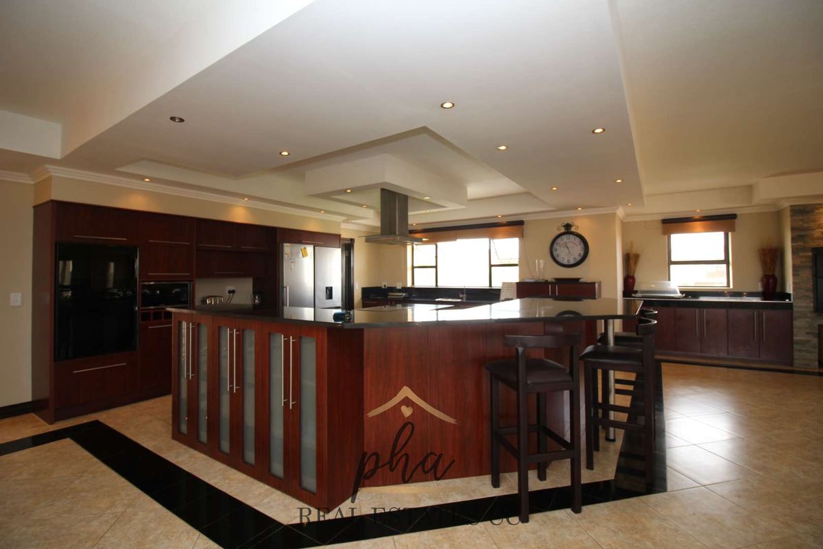 Spacious kitchen featuring dark wood cabinetry, granite countertops, a central island with breakfast bar, and integrated stainless steel extractor fan.