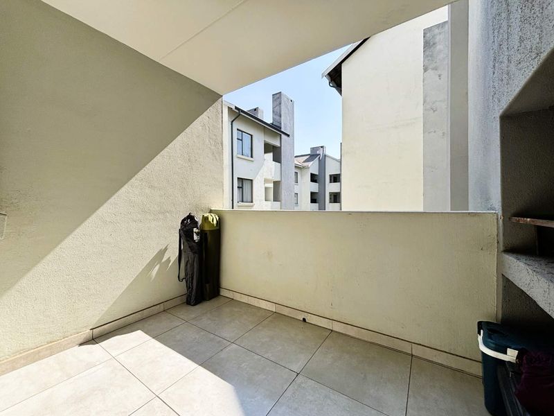 A private balcony featuring tiled flooring and a built-in braai, offering an open outdoor space with views of the surrounding apartment complex.