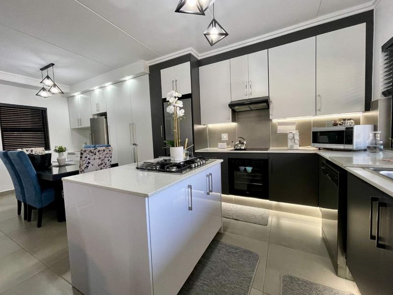Modern open-plan kitchen featuring a central island with gas hob, sleek two-tone cabinetry, stone countertops, and integrated lighting, seamlessly flowing into the dining area.