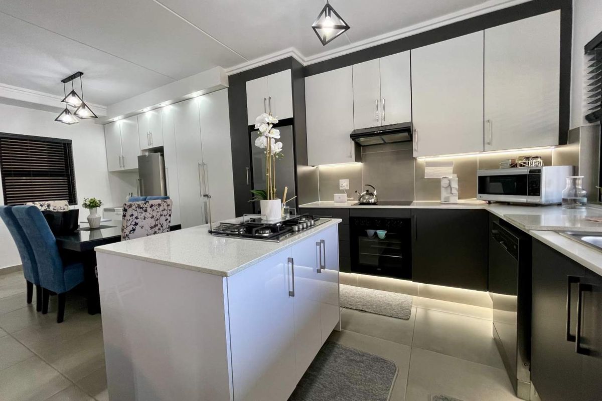 Modern open-plan kitchen featuring a central island with gas hob, sleek two-tone cabinetry, stone countertops, and integrated lighting, seamlessly flowing into the dining area.