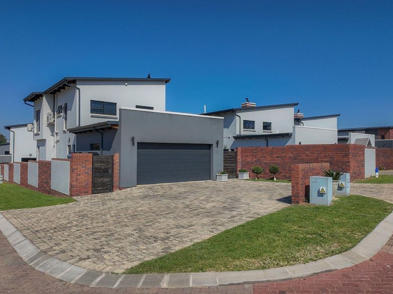 Modern double-story residential property featuring a paved driveway, secure double garage, and attractive brick boundary walling in a well-maintained estate setting.