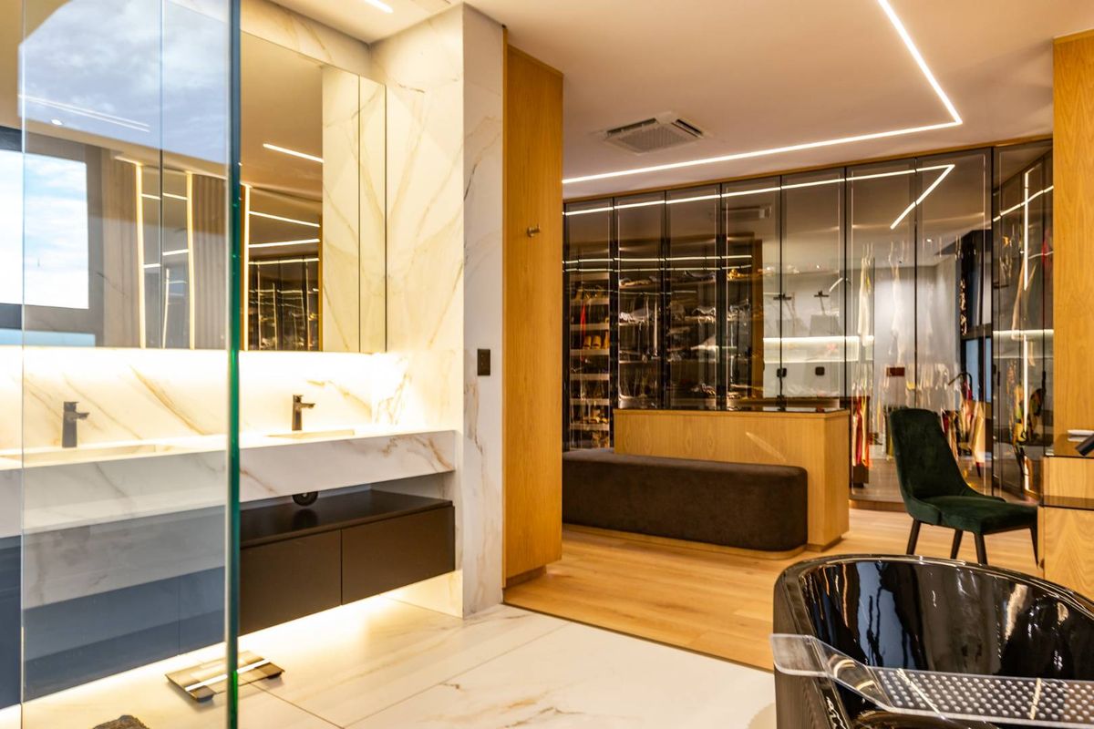 Modern open-plan bathroom and dressing area featuring marble-look tiling, dual vanity, integrated lighting, and extensive glass-fronted wardrobe cabinetry.