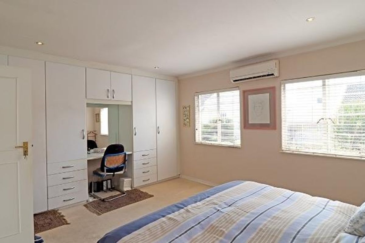 Spacious bedroom featuring extensive built-in cabinetry with integrated vanity, recessed ceiling lighting, and a wall-mounted air conditioning unit.